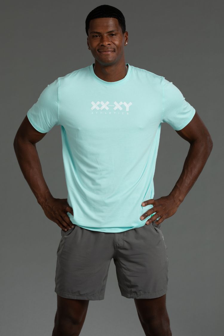 Man wearing a light blue t-shirt with a logo and gray shorts on a gray background || Aqua Heather