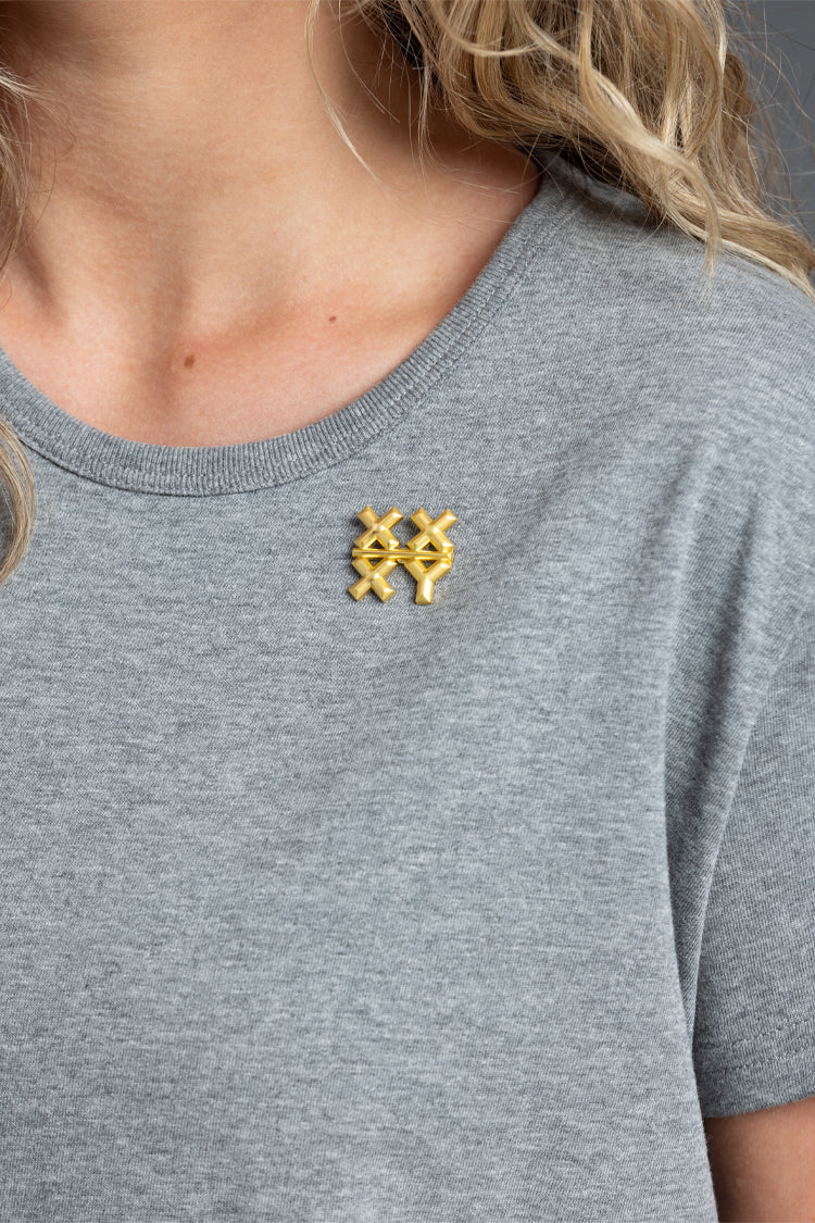 Person wearing a gray t-shirt with a gold XXXY pin