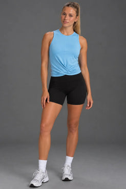 Woman wearing a light blue twist-front performance tank with black bike shorts. || Light Blue