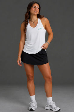 Woman standing in a studio with a gray background wearing a white tank top with a "XX-XY ATHLETICS"  logo || White