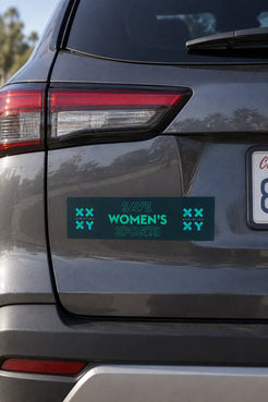 A rectangular bumper sticker with the text 'SAVE WOMEN'S SPORTS' in teal on a dark teal background, displayed on the rear bumper of a gray SUV.