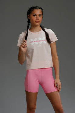 Woman wearing a light-colored t-shirt with a graphic design and pink shorts on a gray background || Light Pink