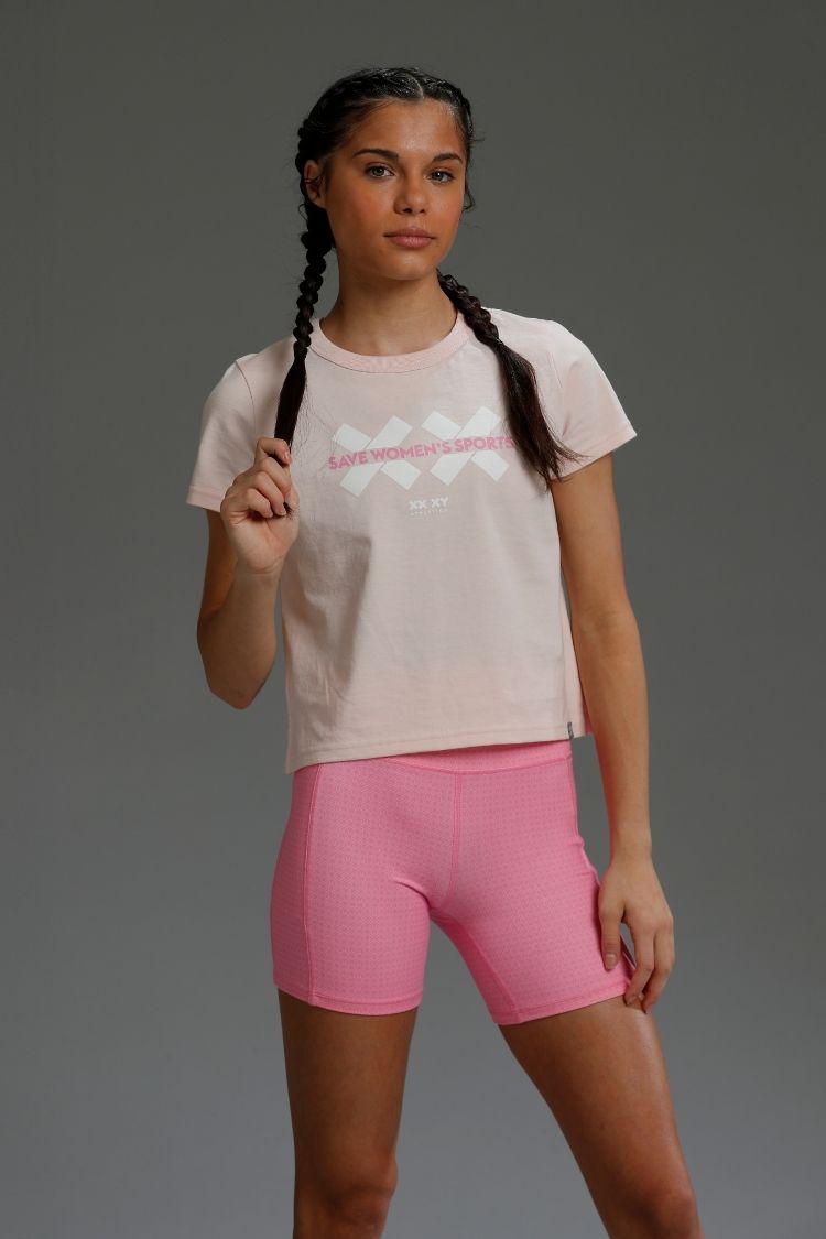 Woman wearing a light-colored t-shirt with a graphic design and pink shorts on a gray background || Light Pink