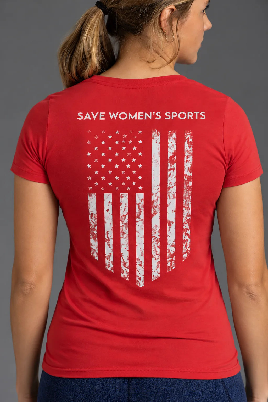 Close-up of the back of a red XX-XY Athletics T-shirt featuring the white Save Women's Sports slogan above a distressed American flag graphic.