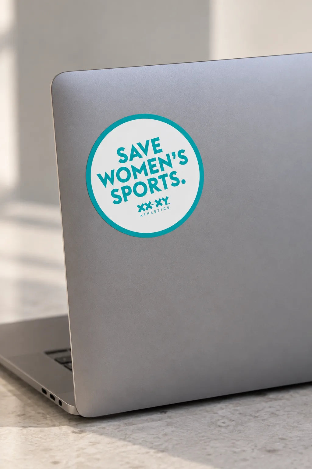 Round Save Women’s Sports XX-XY Athletics sticker on the back of a silver laptop.
