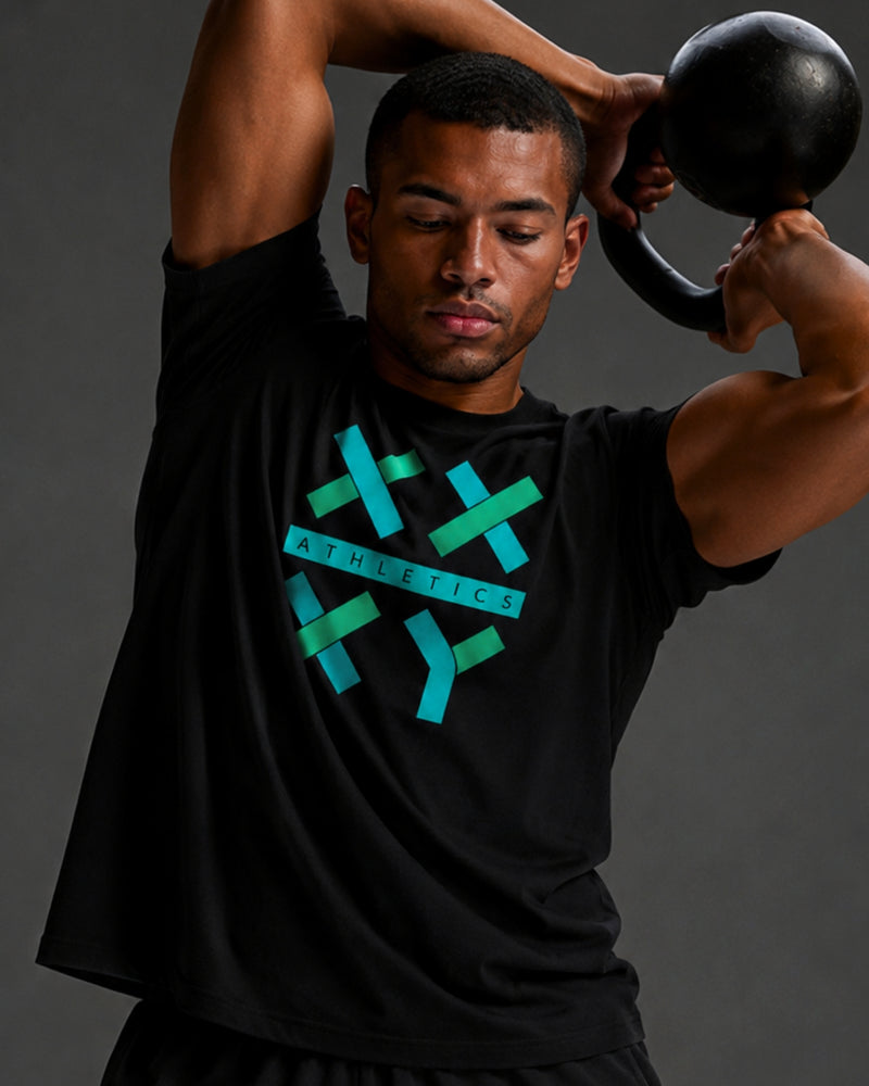 A man lifting a kettlebell while wearing a black athletic t-shirt with a teal and green geometric logo that reads 'ATHLETICS'.