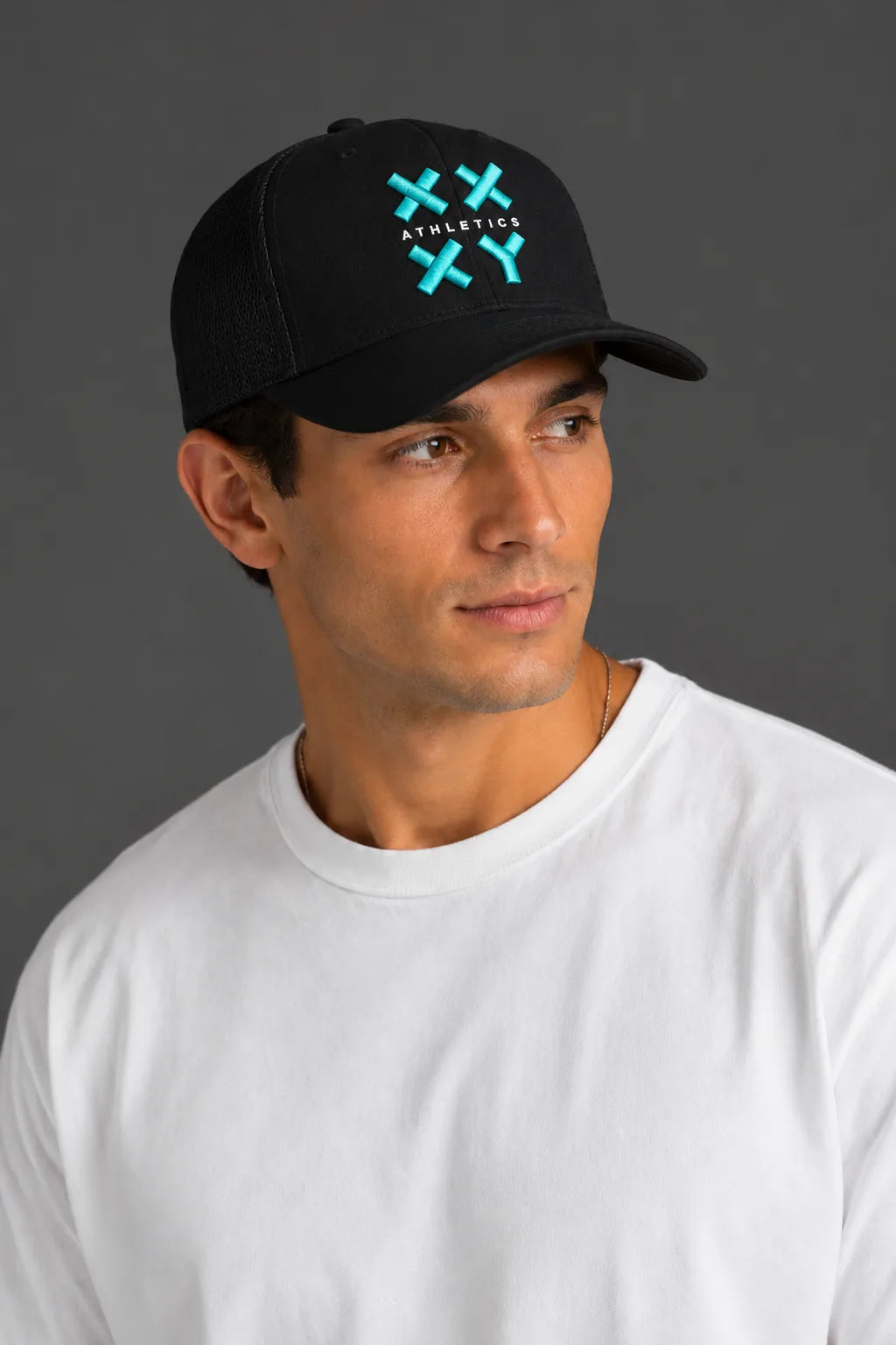 A man wearing a black baseball cap with a green and white embroidered logo that reads 'ATHLETICK' and 'XX', paired with a plain white t-shirt, set against a solid dark gray background. || Black with Color Logo