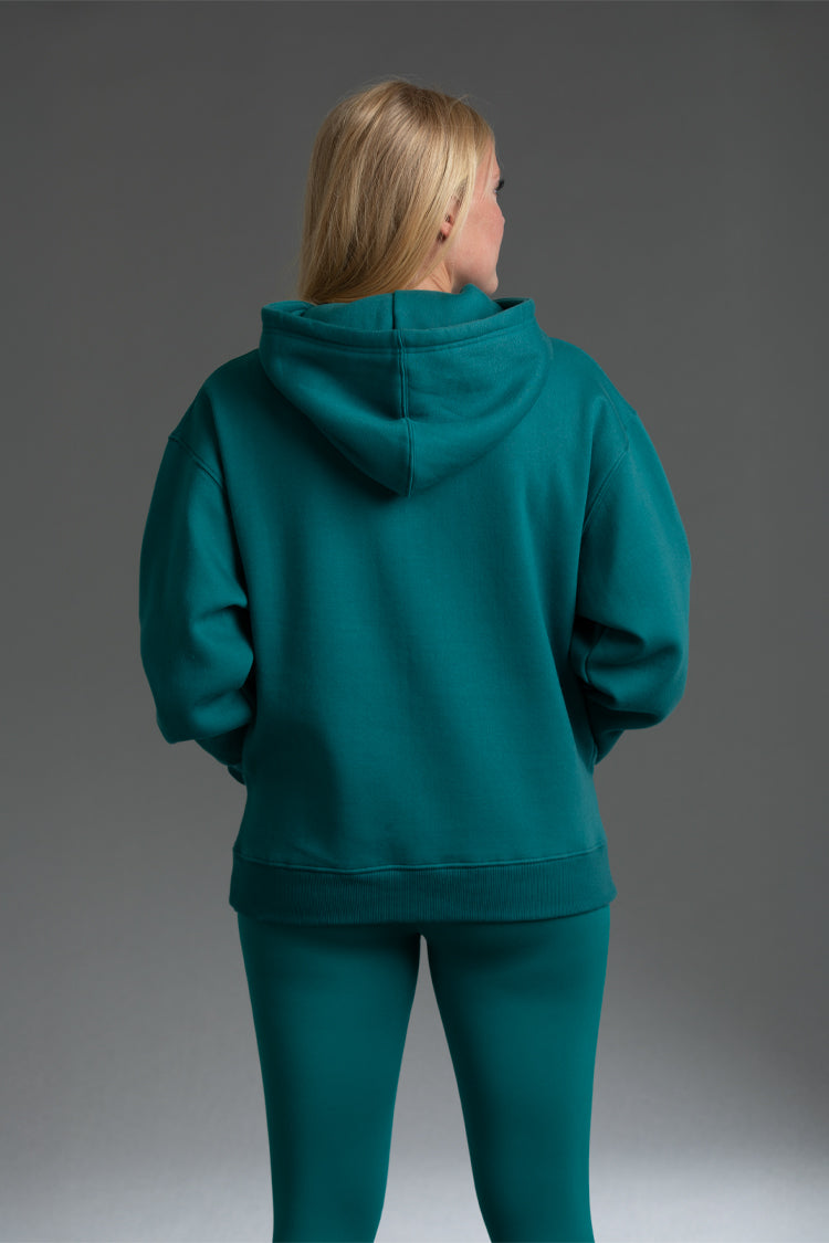 Person wearing a teal hoodie and pants on a gray background || teal
