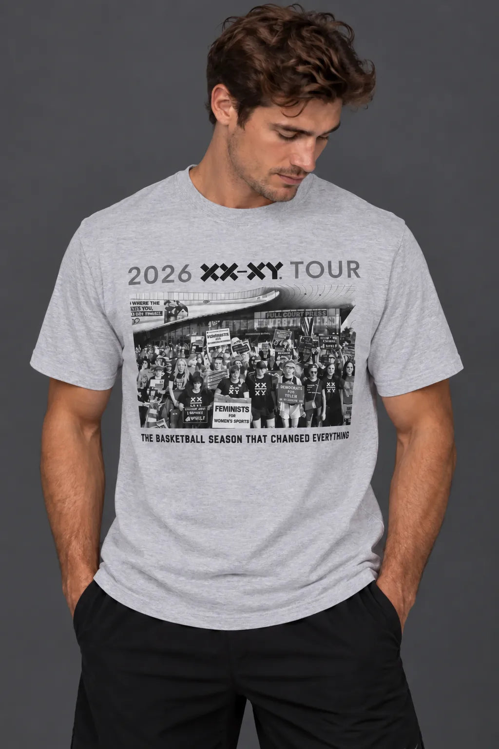 A man wearing a gray short-sleeve graphic t-shirt with a black and white basketball-themed print on the front, paired with black pants, against a dark gray studio background. || Light Heather Gray