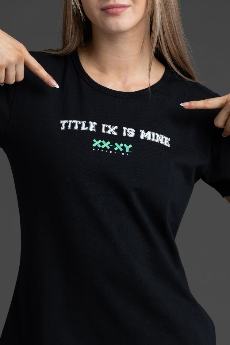 Person wearing a black t-shirt with 'TITLE IX IS MINE' text and pointing to it. || Black