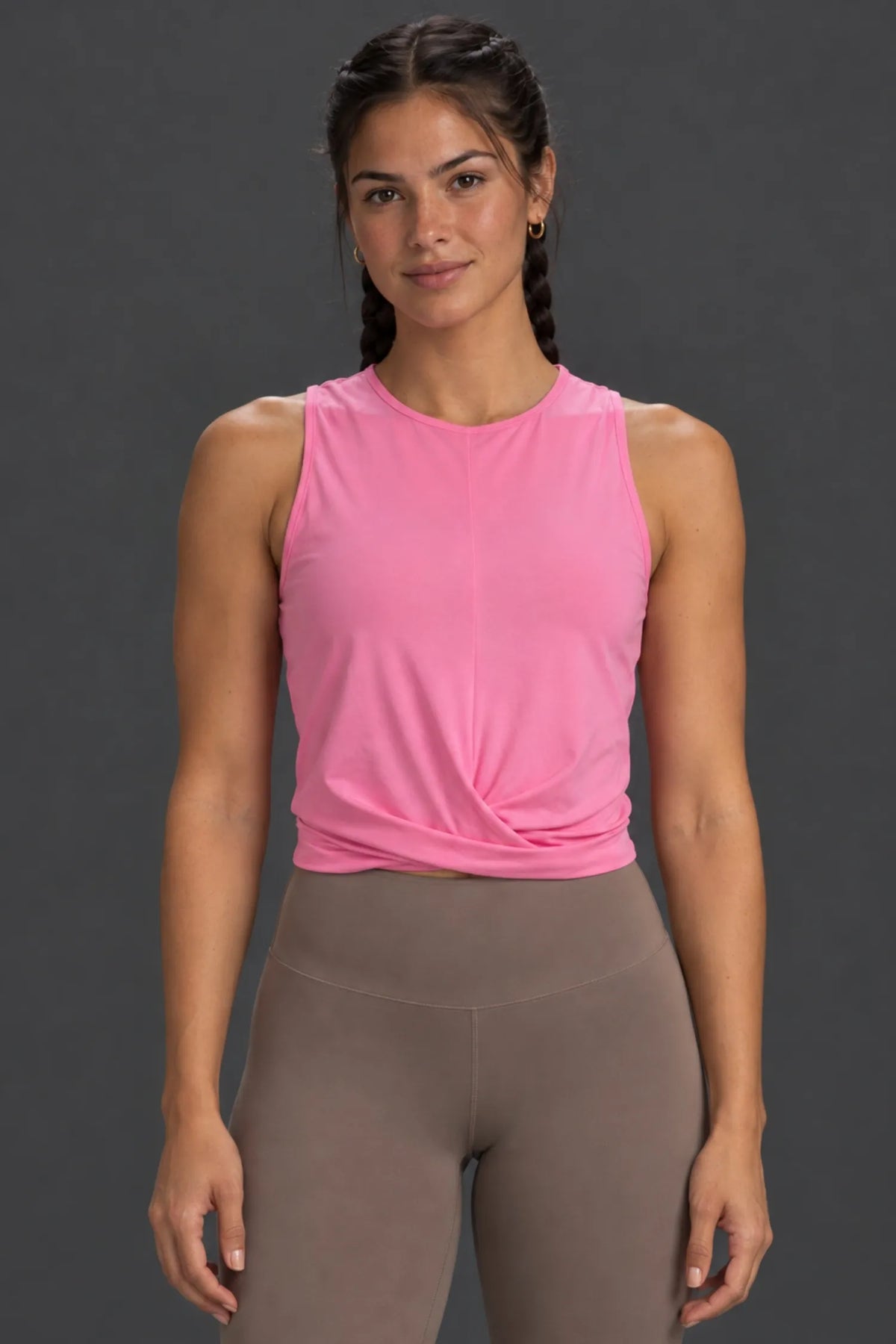 Woman wearing a pink twist-front performance tank with mocha leggings.