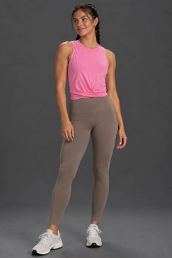 Woman wearing a pink twist-front performance tank with mocha leggings and white sneakers. || Pink