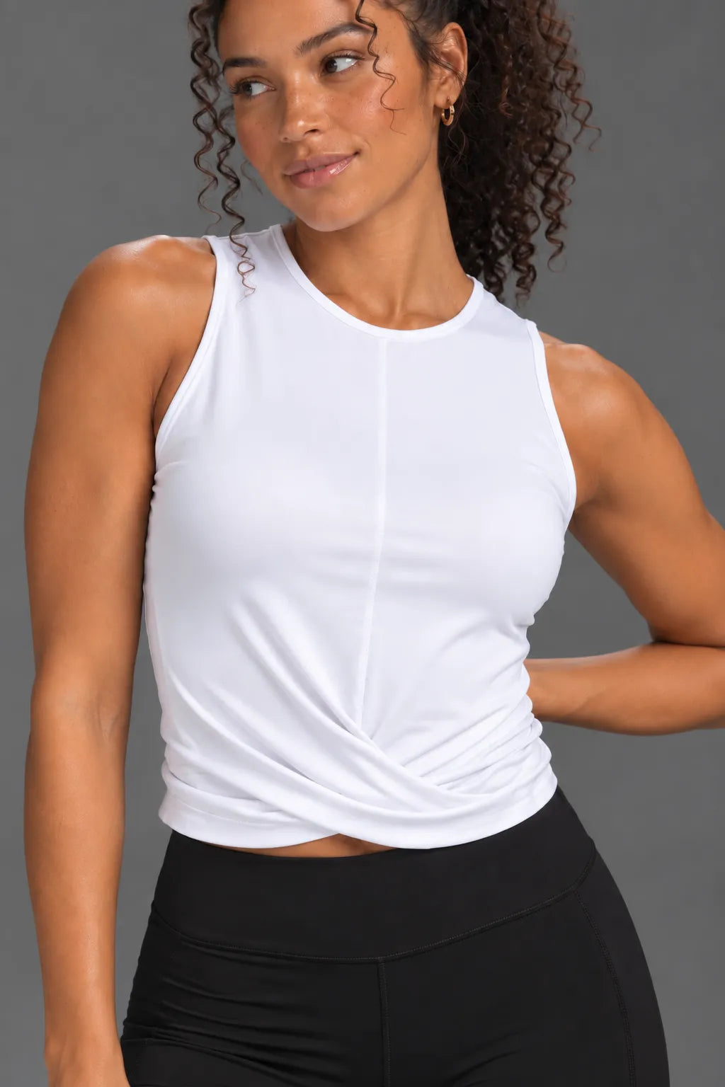 Close-up of woman wearing a white twist-front performance tank with black bike shorts. || White