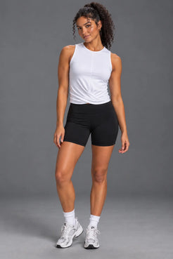 Woman wearing a white twist-front performance tank, black bike shorts and white sneakers. || White