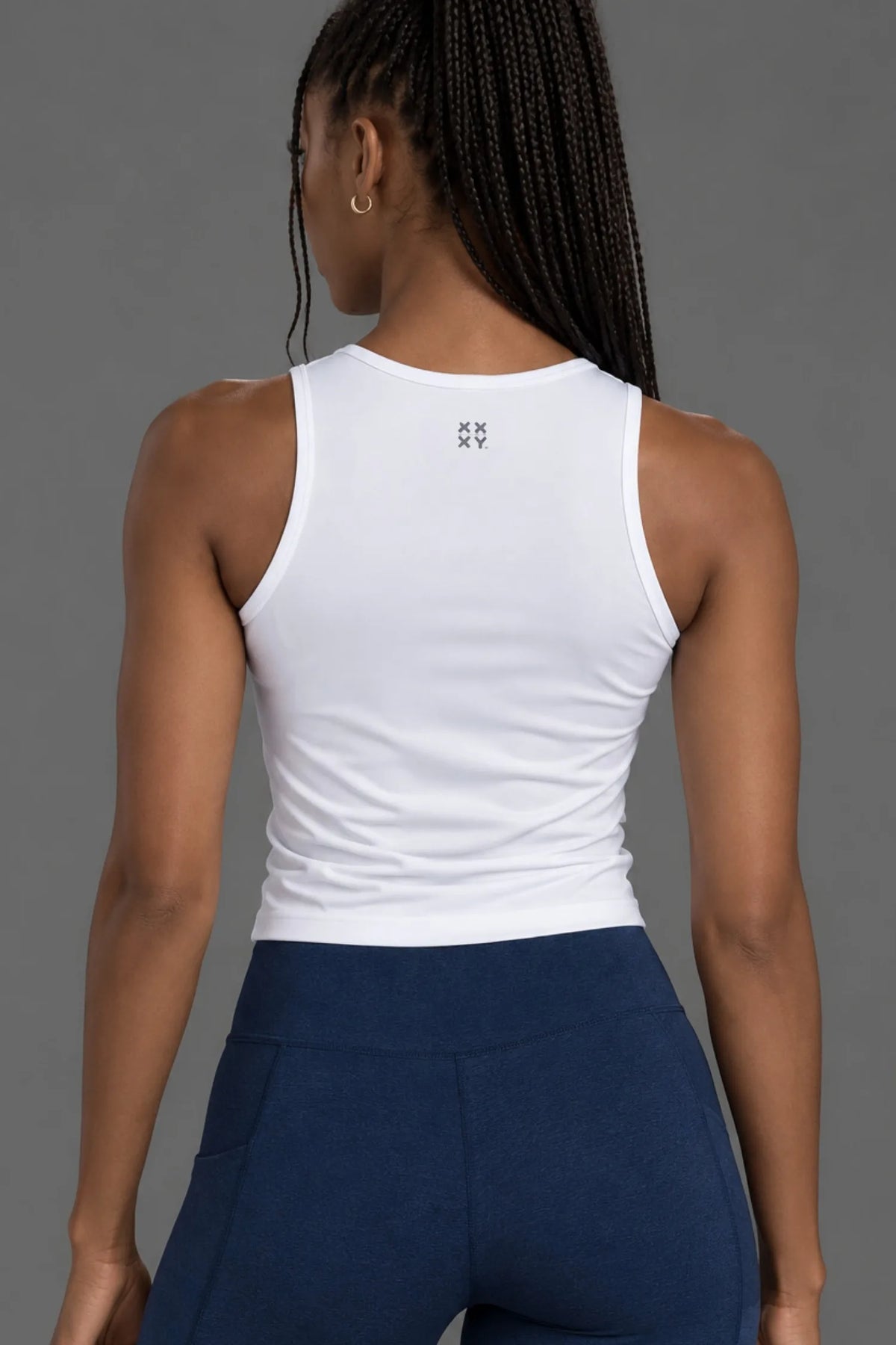 Back view of female model wearing a white XX-XY Athletics tank top with navy leggings.