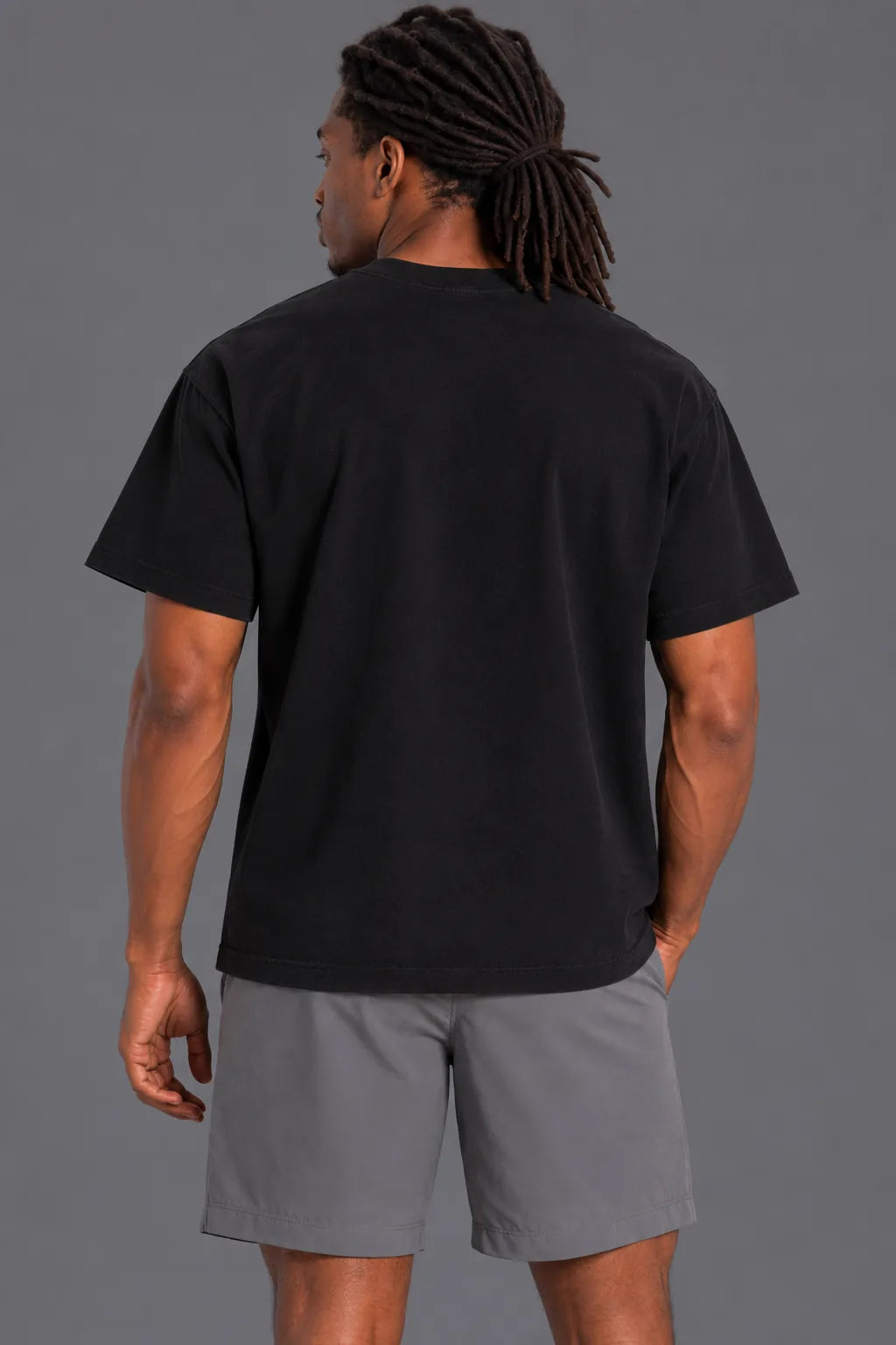 Back view of male model wearing the black XX-XY Athletics T-shirt with gray shorts on a gray studio background.