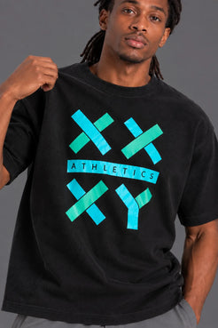Male model wearing the black XX-XY Athletics graphic T-shirt with teal logo on a gray studio background. || Black
