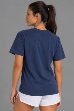 Female model showcasing the plain back of the XX-XY Athletics Varsity Logo Tee, paired with white athletic shorts and a slicked-back ponytail || Navy