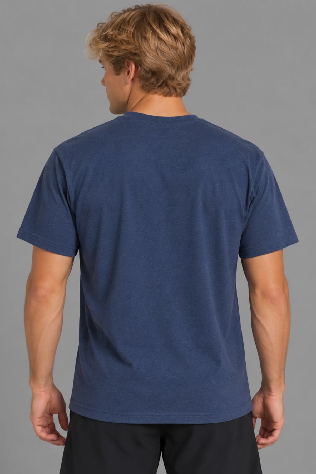 Male model showcasing the plain back of the XX-XY Athletics Varsity Logo Tee, paired with black shorts against a gray studio background || Navy