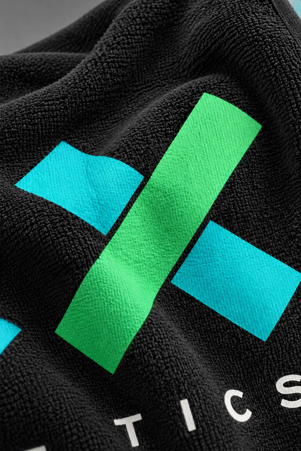Close-up of the black XX-XY Athletics golf towel highlighting the soft terry cloth texture and vibrant turquoise and green printed logo