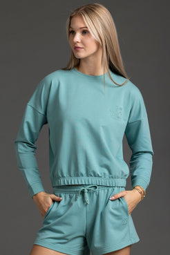 Woman wearing a teal sweatshirt and shorts set against a gray background || Underseas