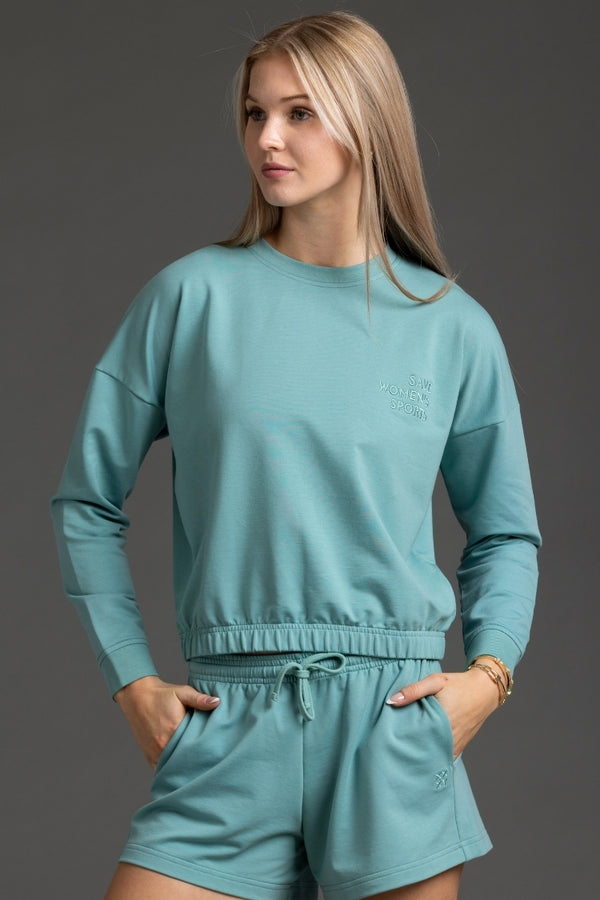 Woman wearing a teal sweatshirt and shorts set against a gray background || Underseas