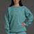 Woman wearing a teal sweatshirt and shorts with a logo on a gray background || Underseas
