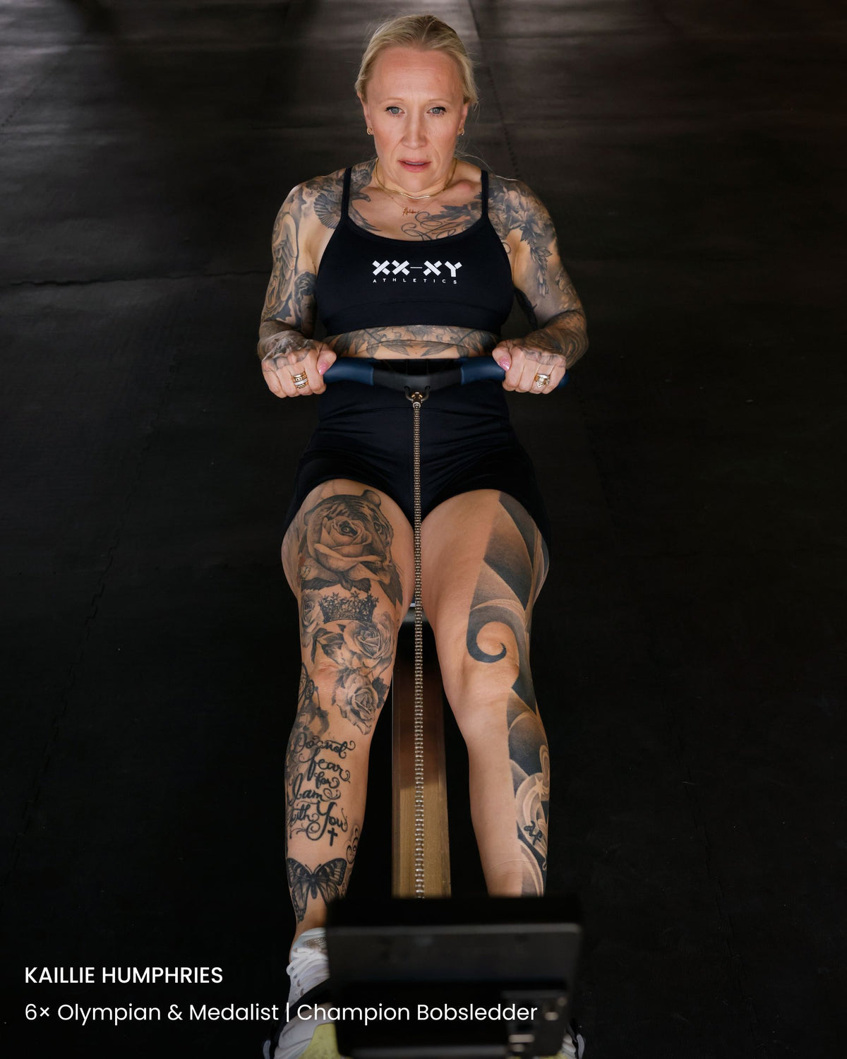 Woman with tattoos using a piece of exercise equipment against a black background