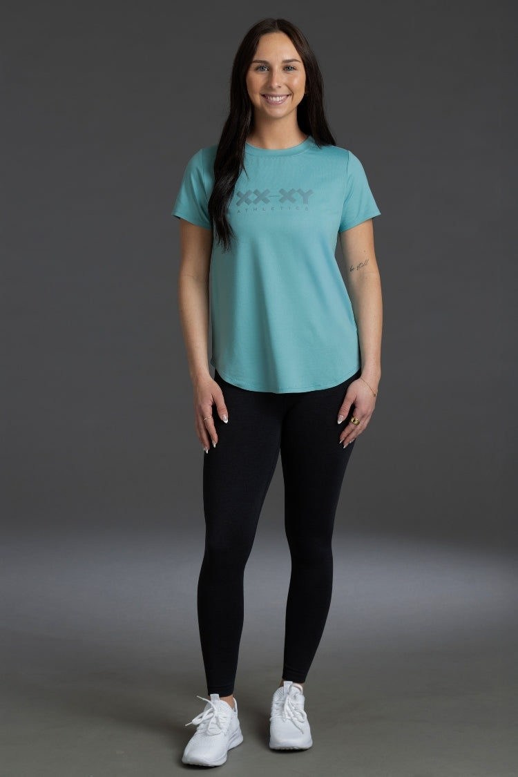 Woman wearing a teal t-shirt with text and black leggings on a gray background