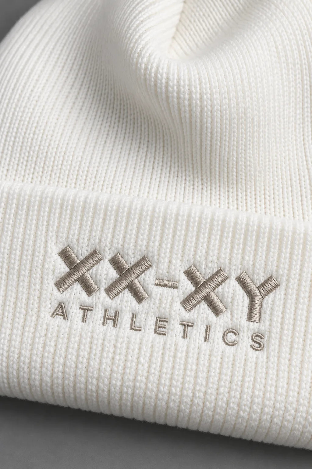 Close-up of white ribbed knit beanie highlighting the XX-XY Athletics embroidered logo and fabric texture