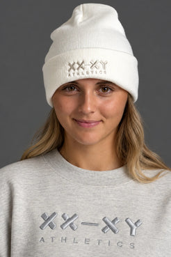 Female model wearing white XX-XY Athletics embroidered beanie and gray crewneck sweatshirt against a gray background || White