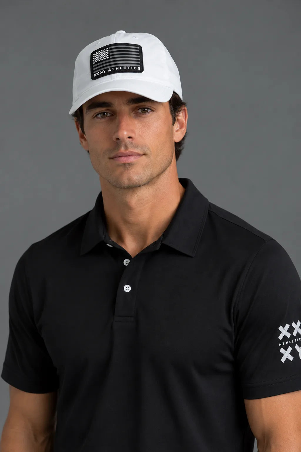 A man wearing a white baseball cap with a black American flag patch and 'WORLD ATHLETICS' text, paired with a black polo shirt featuring a white logo on the sleeve, against a solid gray background.