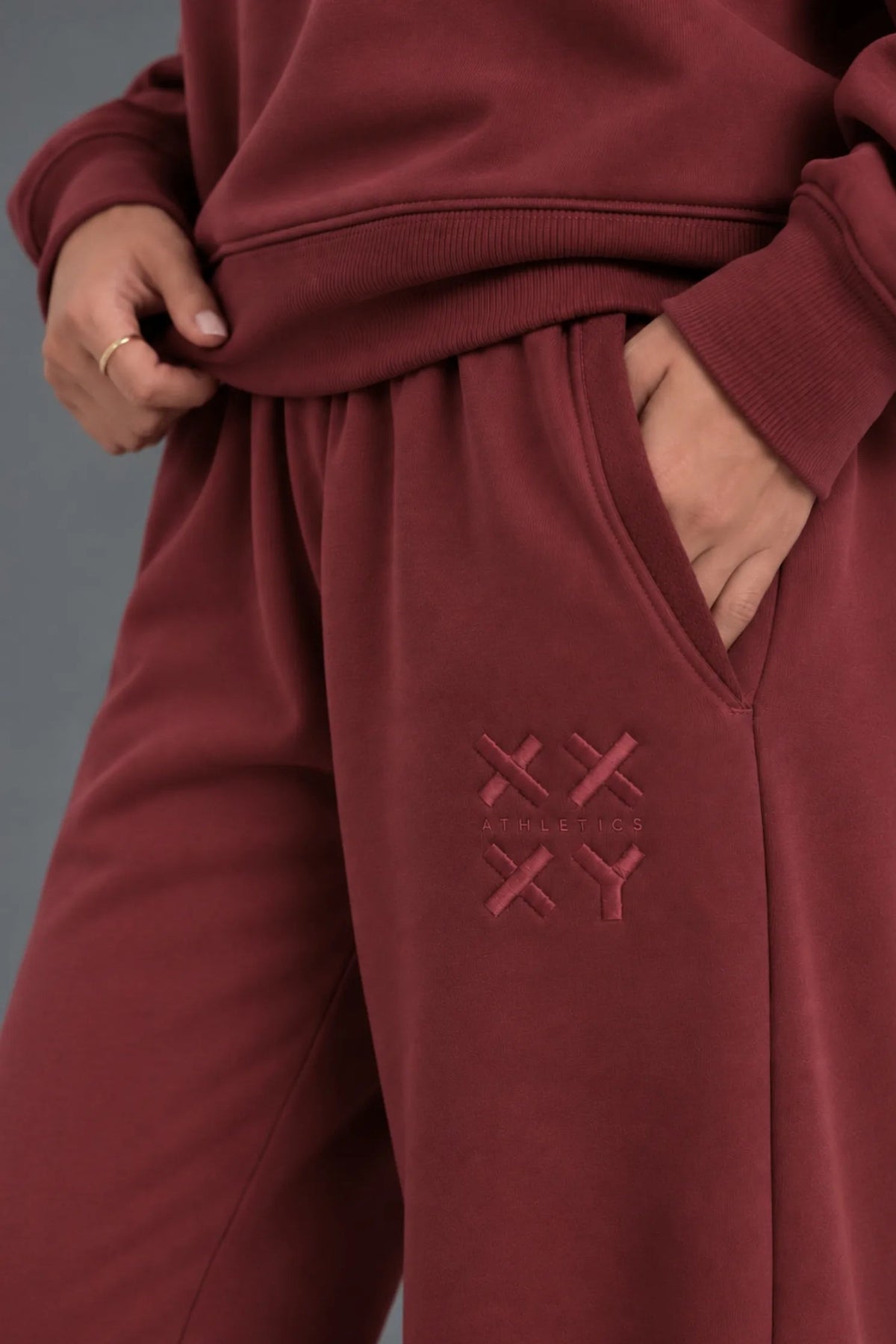 Close-up of burgundy XX-XY Athletics sweatpants showing textured pocket lining and tonal embroidered logo. || Red Wine