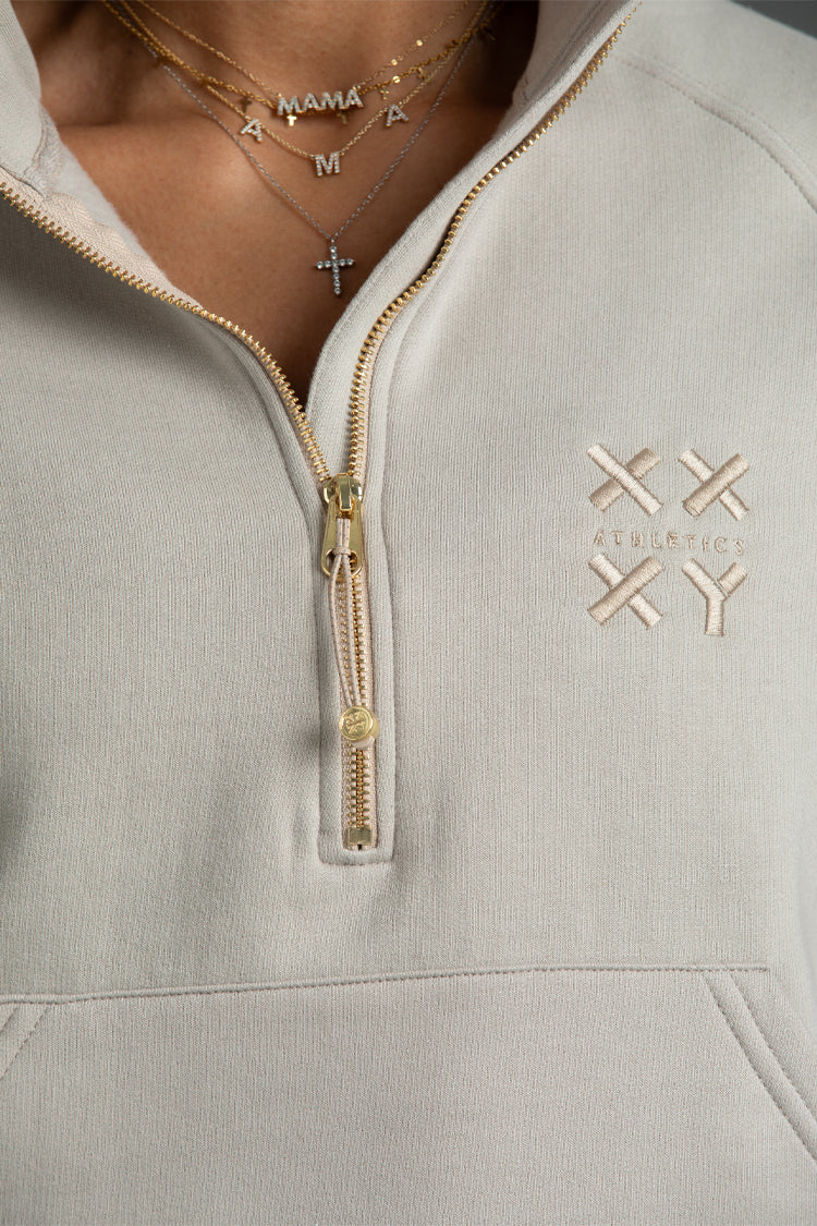 Taupe hoodie with gold zipper and 'XXXY' logo on chest, worn by a person. || Taupe