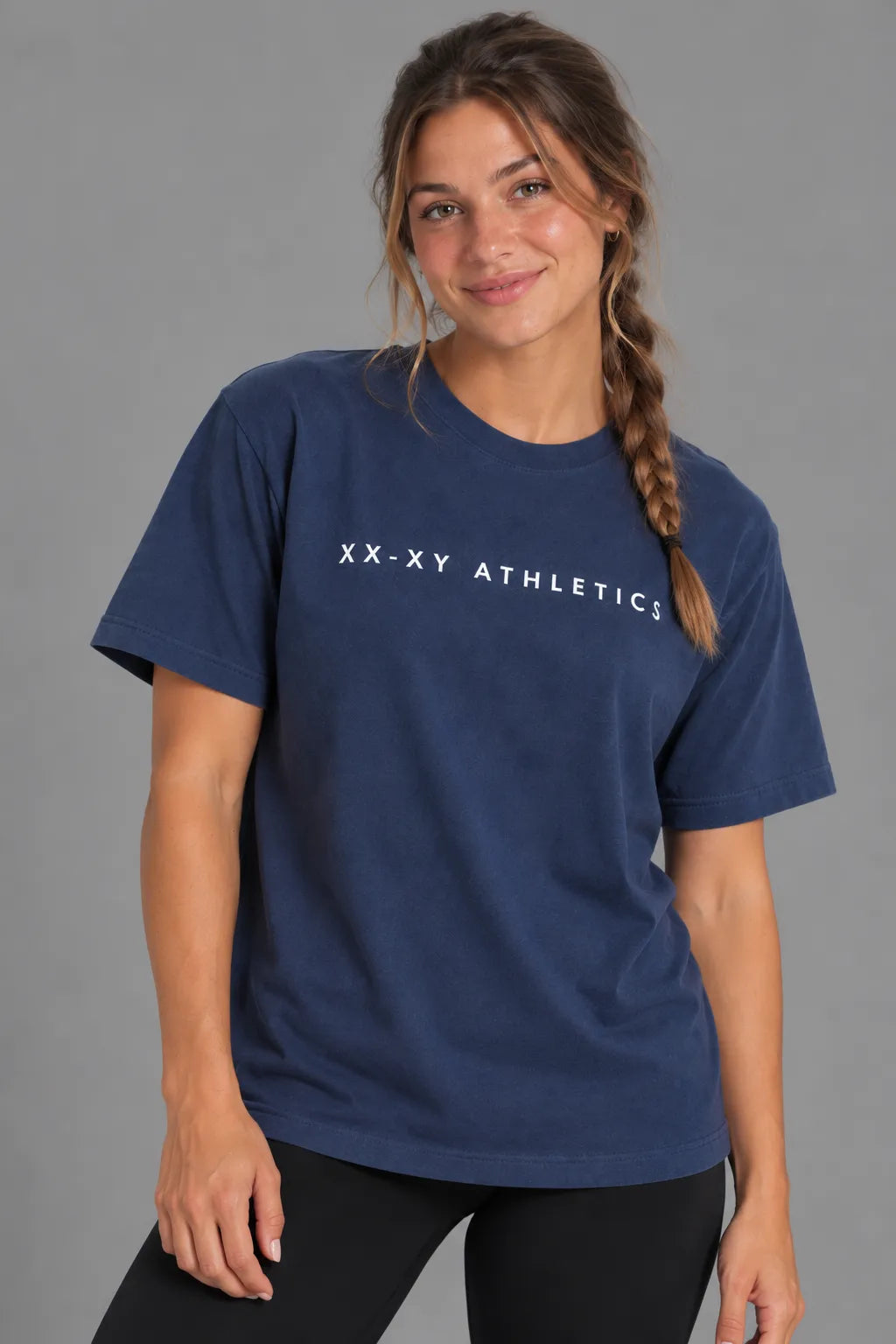 Female model wearing the XX-XY Athletics Wordmark Logo Boyfriend Tee with black leggings, featuring white lettering across the chest