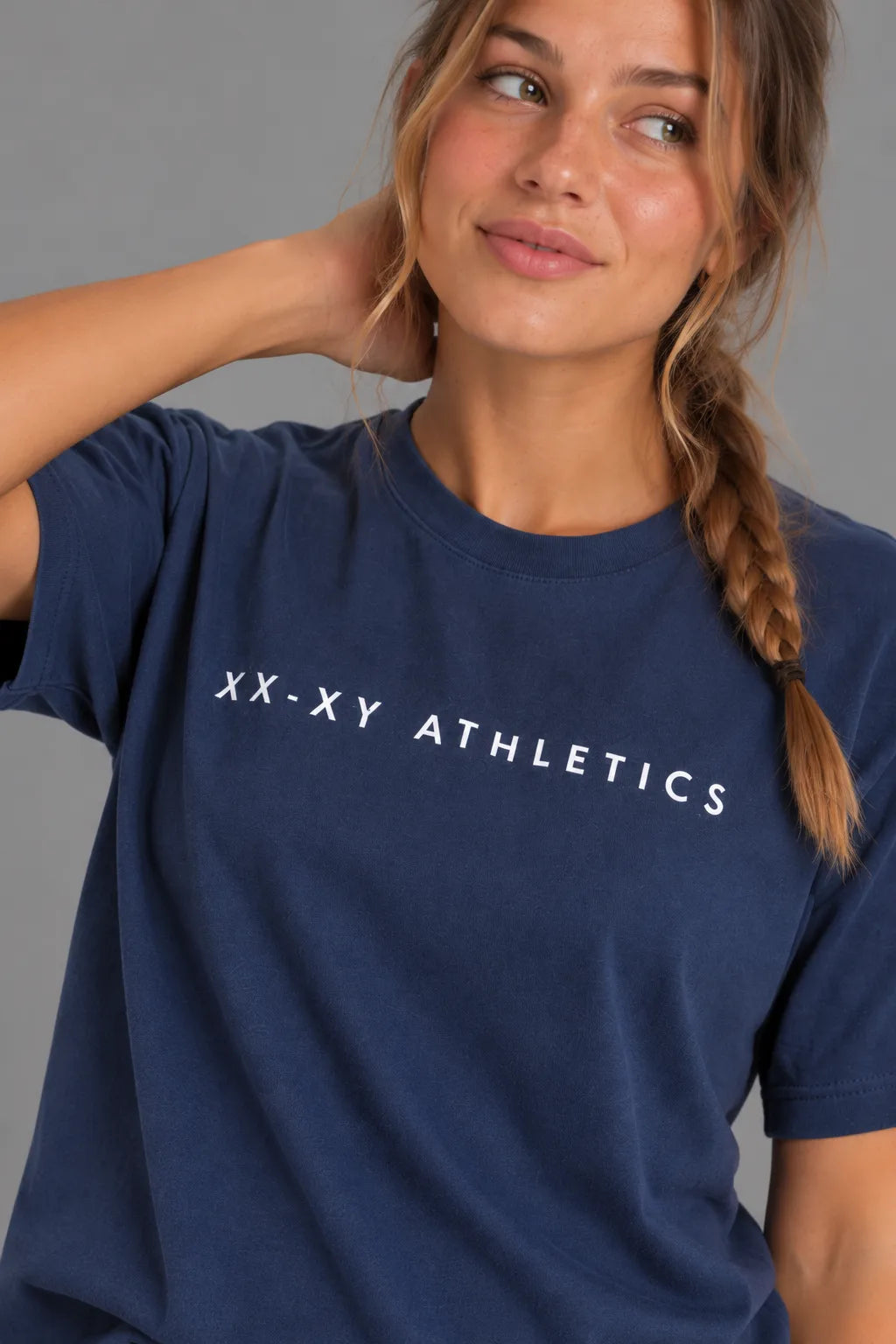 Female model smiling at the camera in the XX-XY Athletics Wordmark Logo Boyfriend Tee, styled with a loose braid and black leggings || Navy