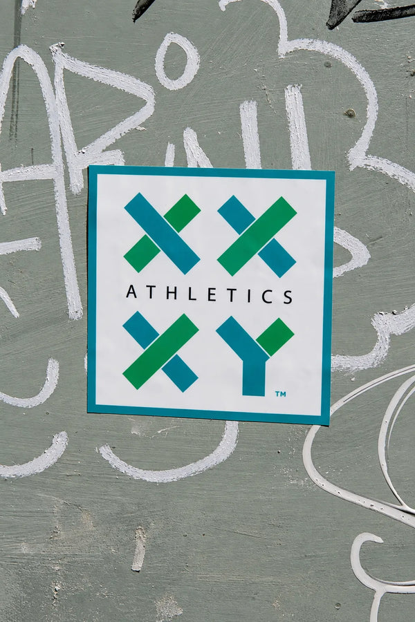 XX-XY Athletics logo sticker displayed on a gray graffiti-covered wall. || White