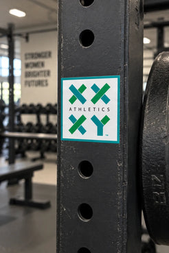 XX-XY Athletics logo sticker displayed on black strength training equipment in a gym. || White