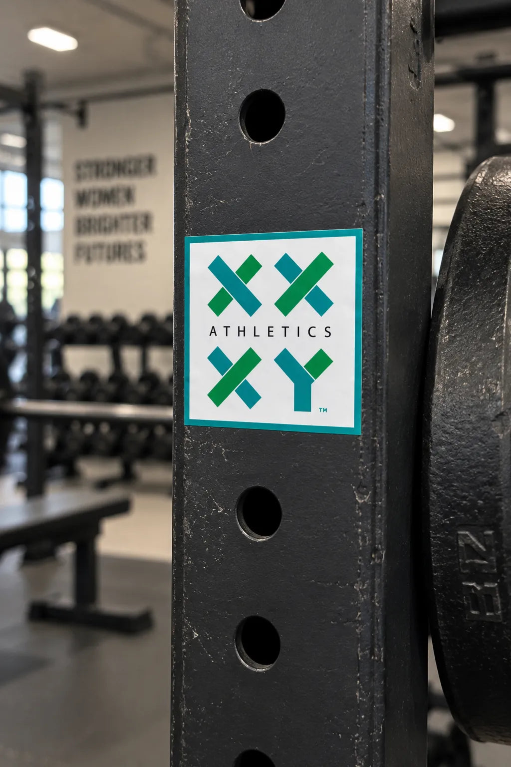 XX-XY Athletics logo sticker displayed on black strength training equipment in a gym. || White