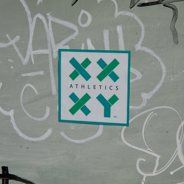 A sticker with the text 'XX-XY Athletics' on a green background, adhered to a surface with some white graffiti. || white