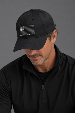 A man wearing a black baseball cap with a black American flag patch and the text 'XXXT ATHLETICS' on the front, paired with a black quarter-zip pullover against a dark gray studio background. || Black