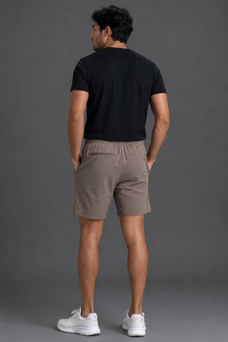 A man wearing taupe-brown athletic shorts with a mint green drawstring, paired with a black t-shirt and white sneakers, shown from the waist down against a gray studio background.