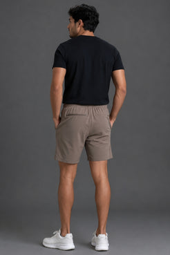 A man wearing taupe-brown athletic shorts with a mint green drawstring, paired with a black t-shirt and white sneakers, shown from the waist down against a gray studio background. || Mocha