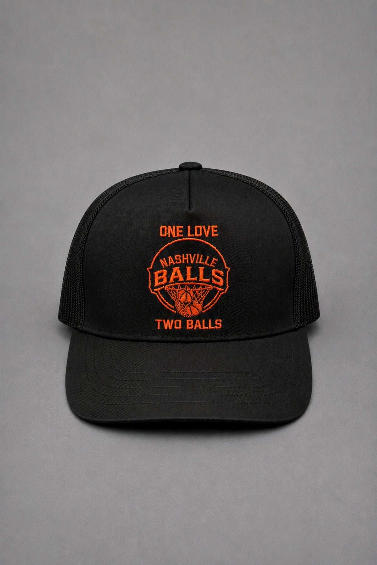 A black trucker-style baseball cap with orange embroidered text and a basketball graphic on the front, photographed against a neutral gray background.