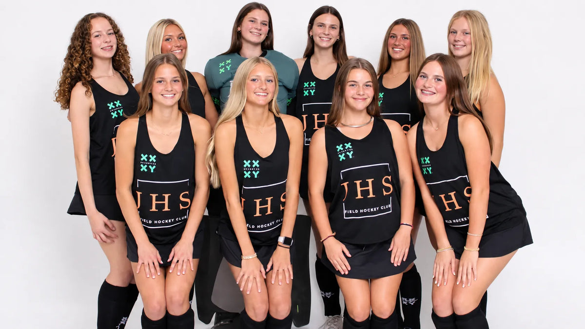 A group of nine female athletes posing together in matching black athletic uniforms with 'XX YX' and 'JHS' printed on the front, set against a plain white studio background.