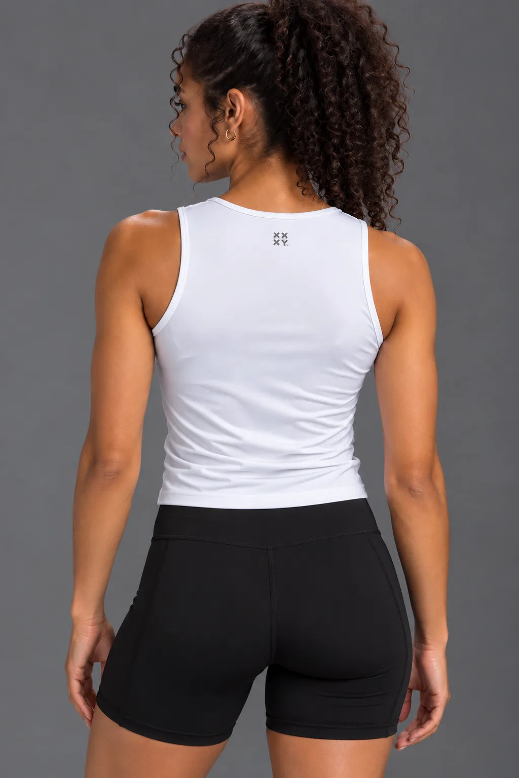 Back view of woman wearing a white performance tank with XX-XY logo and black bike shorts.