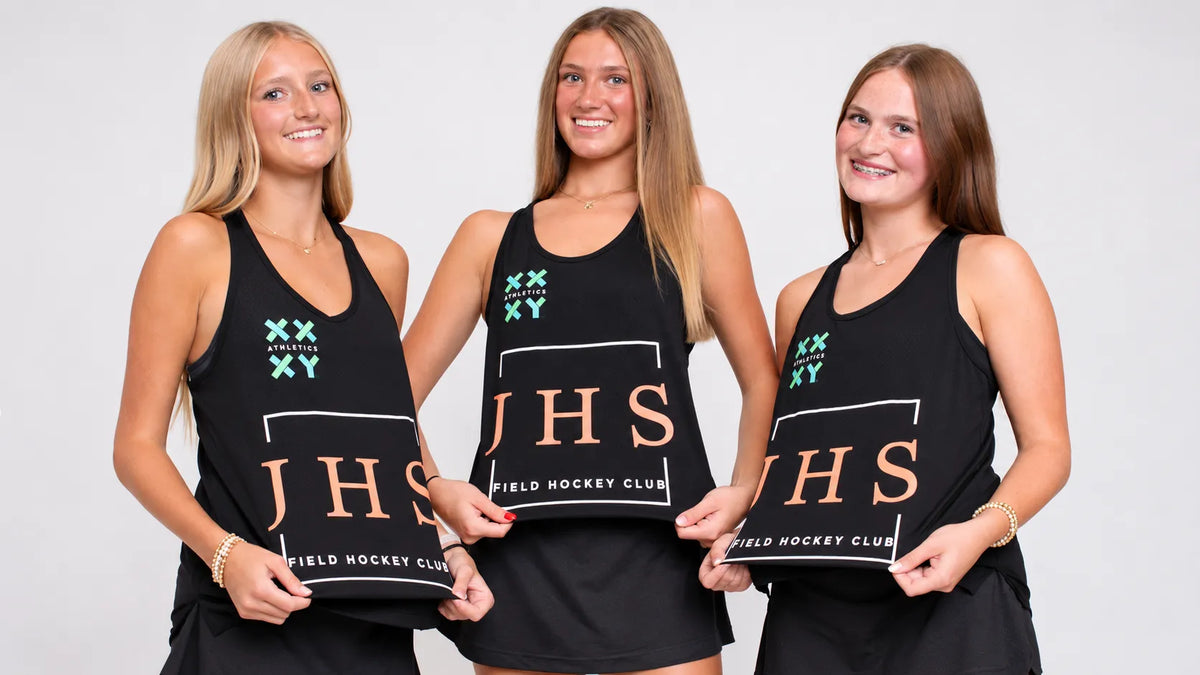 Three women standing side by side wearing matching black athletic tank tops with 'JHS Field Hockey Club' printed in white and teal, holding matching black signs against a light gray studio background.