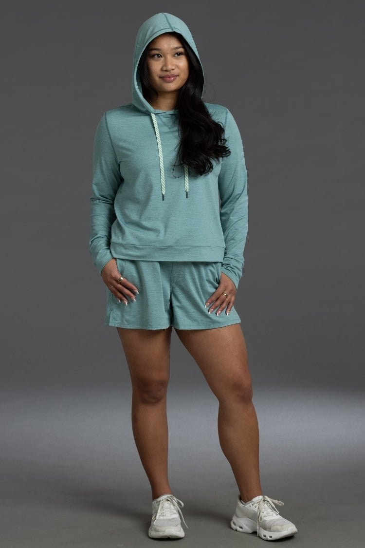 Woman wearing a teal hoodie and shorts set on a gray background